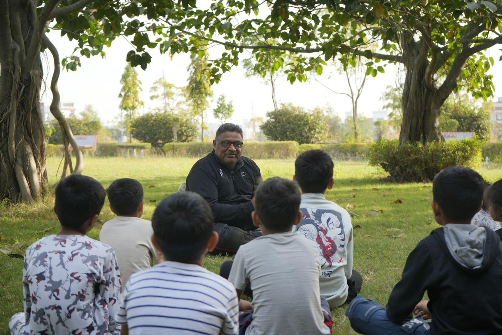 A mentor telling a story to a group of kids under a tree